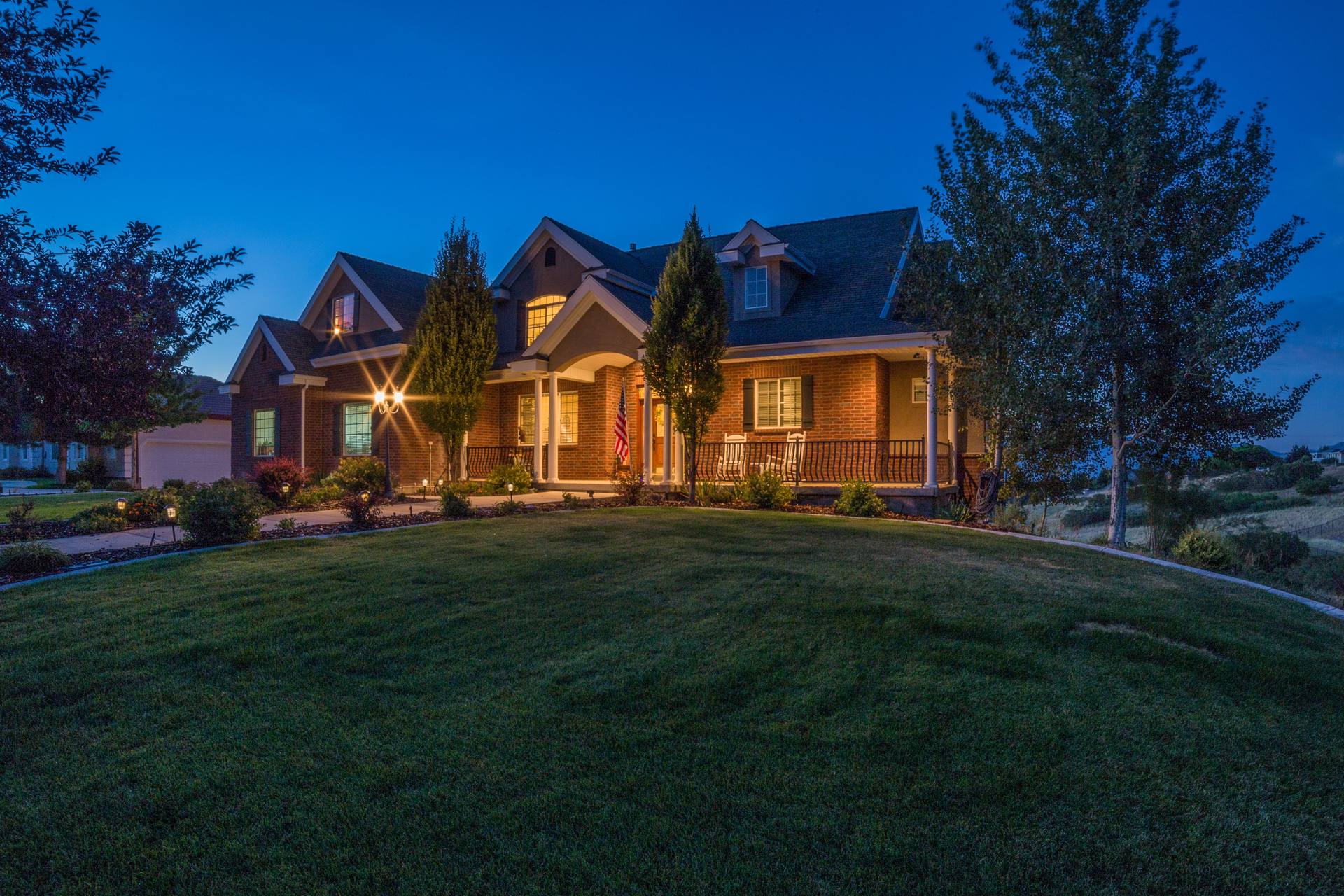 A large craftsman home at blue hour with warm light along the porch and the eaves and the lawn lit from the ground