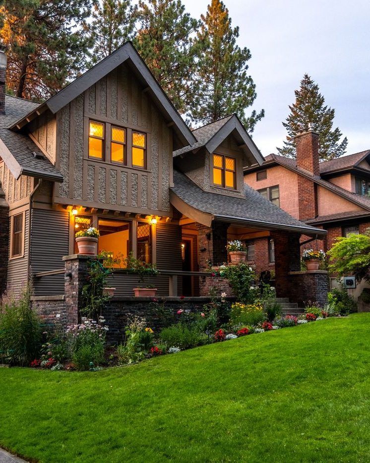 A craftsman home at dusk with warm light through the windows and planted beds along the front