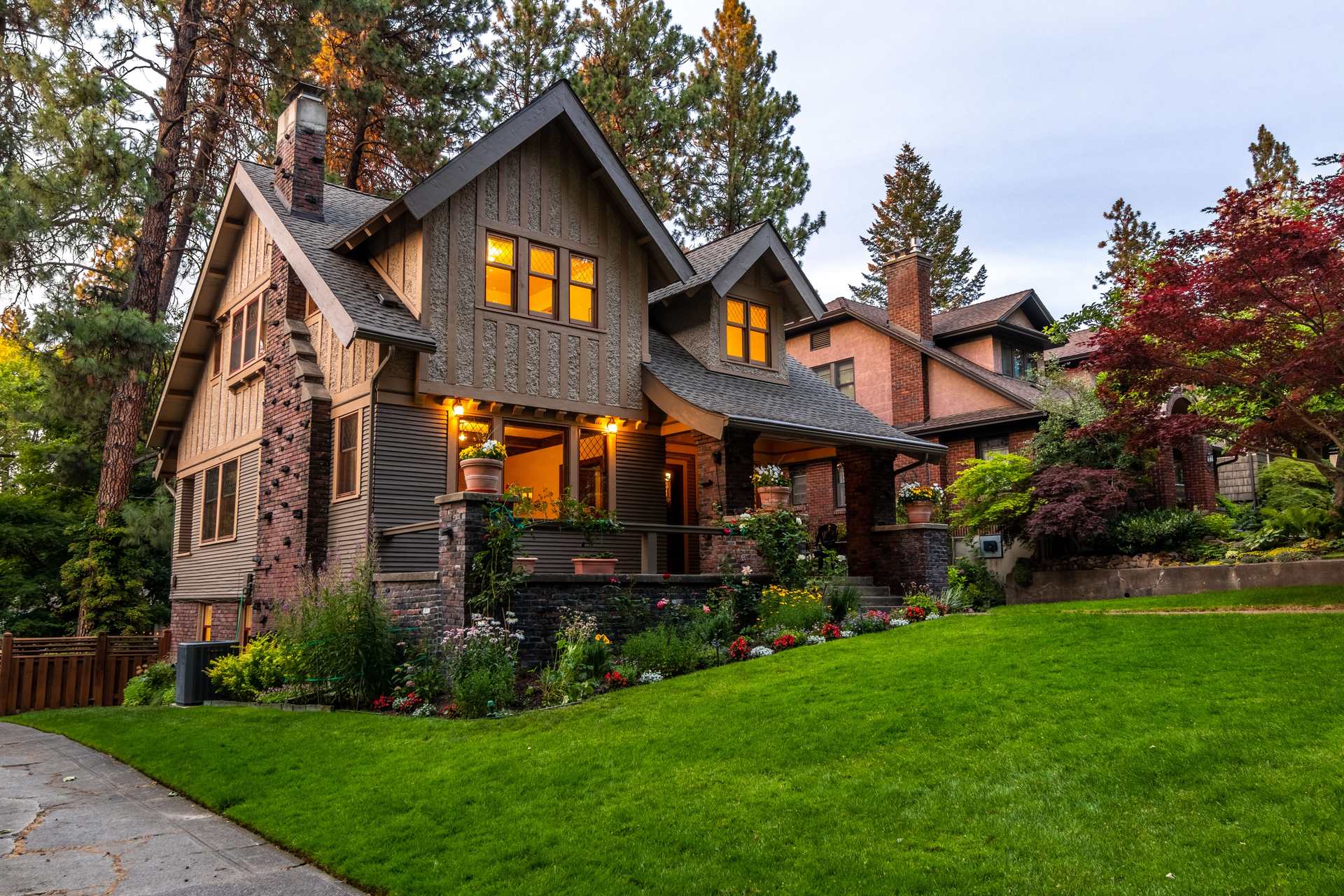 A craftsman home in the evening with warm light along the porch and the eaves and a lit lawn