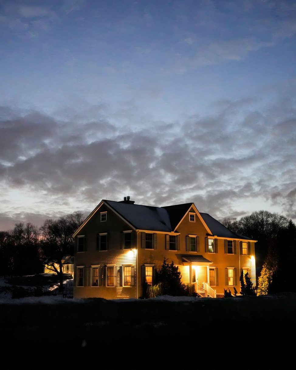A house lit warm against a heavy dusk sky