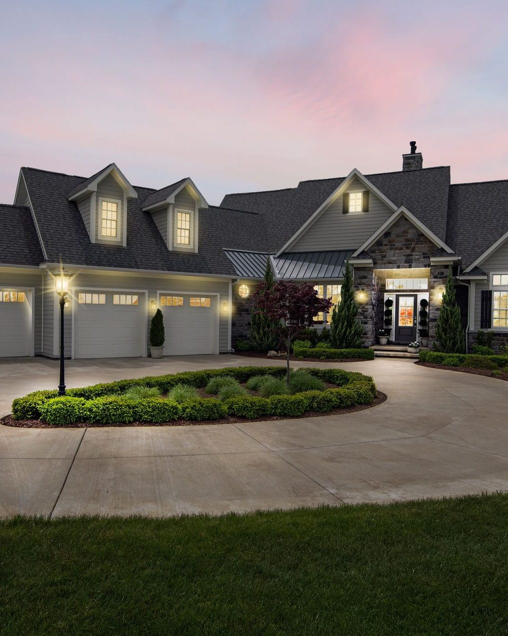 A large house at dusk with the roofline and the beds lit and a circular drive in front