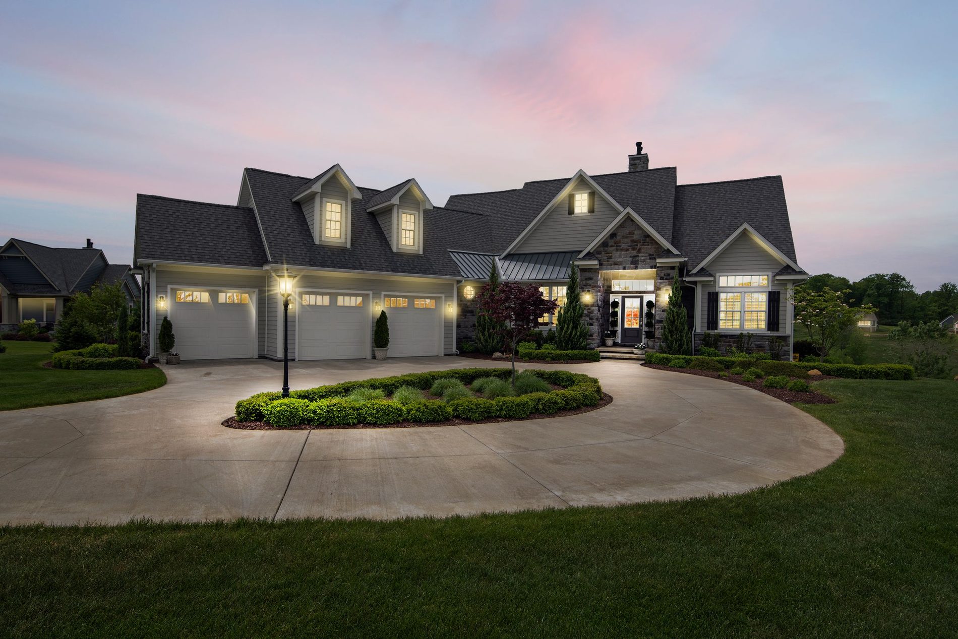 A large property lit from the ground with the trees and the drive picked out