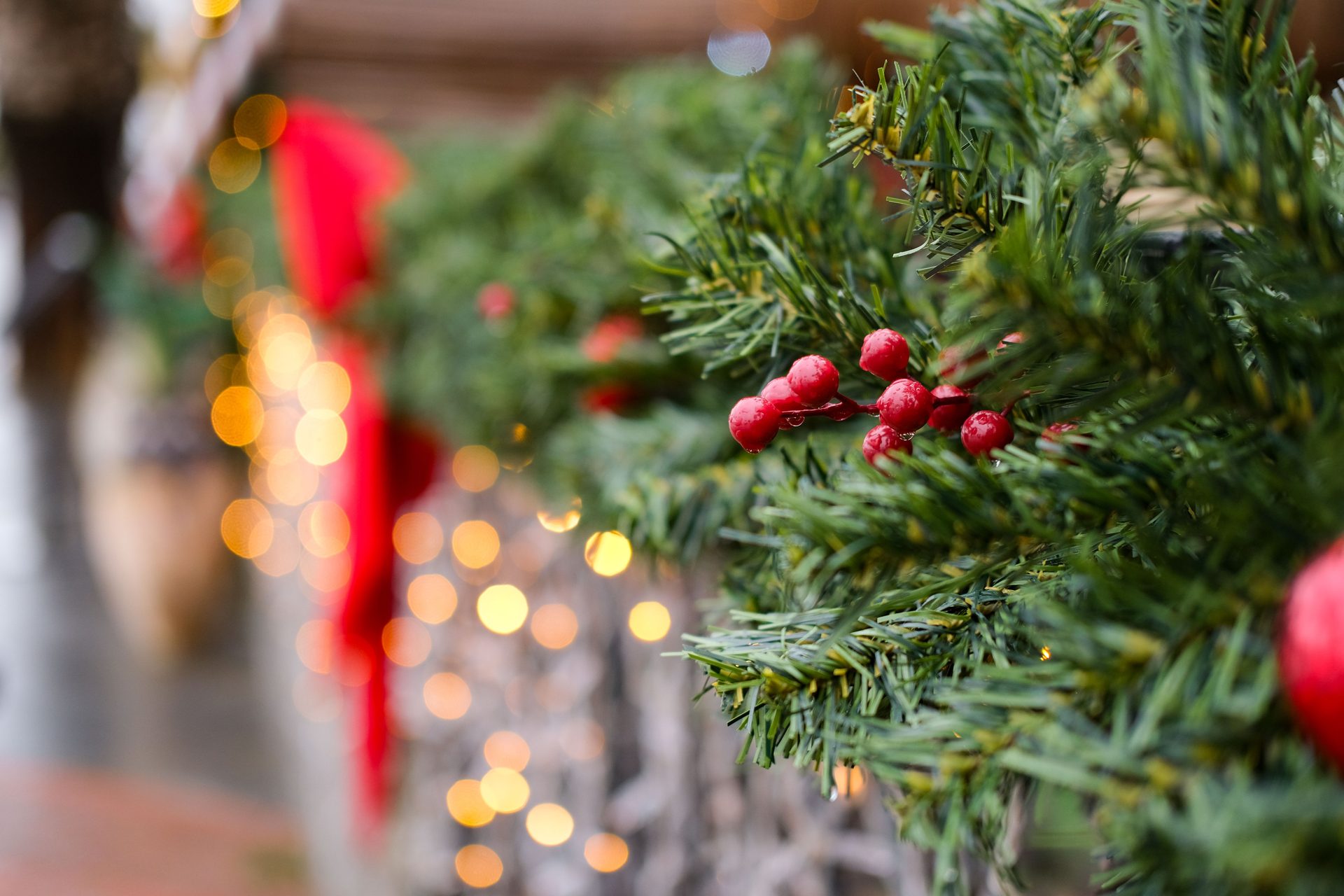 Evergreen garland with a red bow and red berries, lit with warm white bulbs