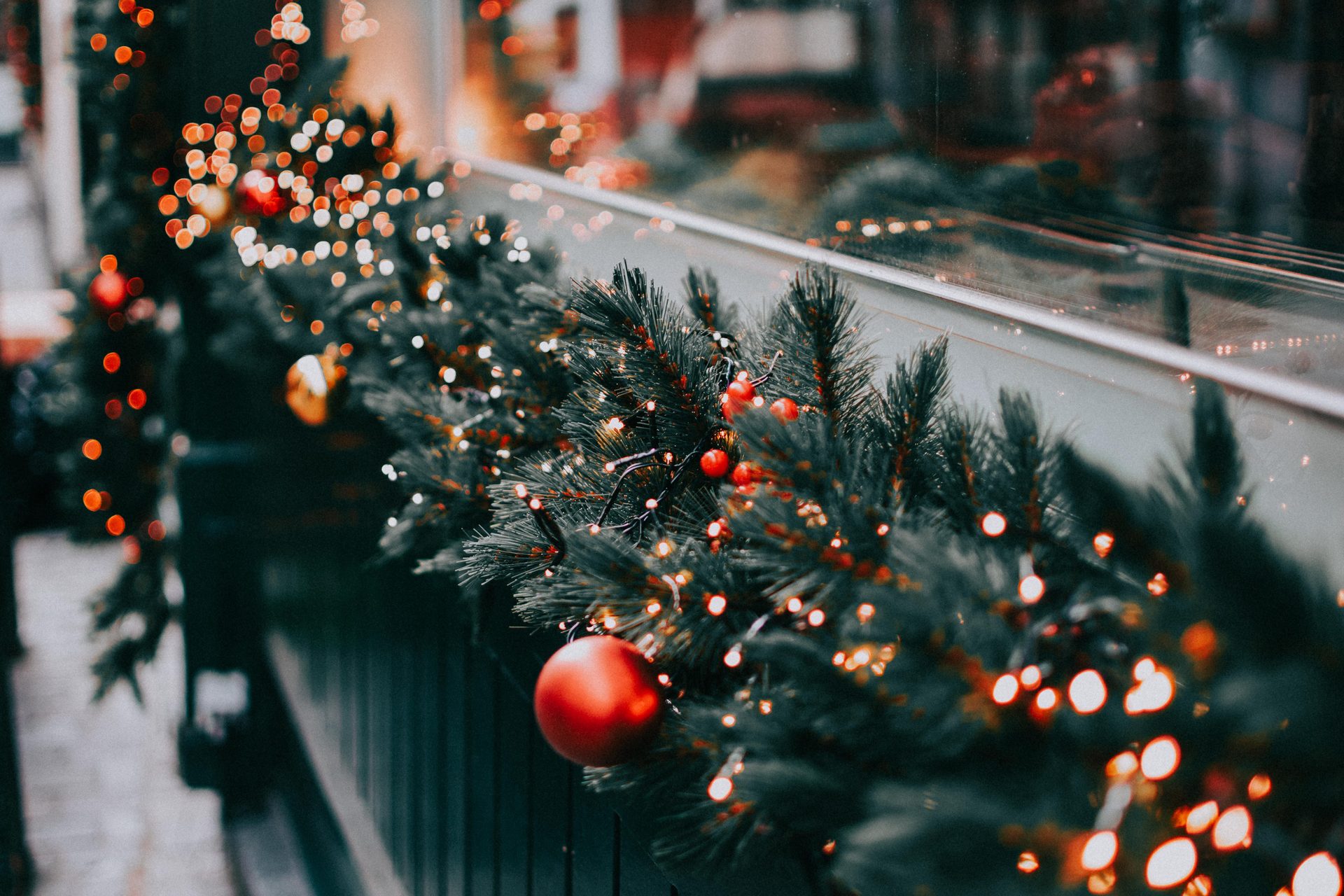 Evergreen garland along a railing, dressed with warm white bulbs and red berries