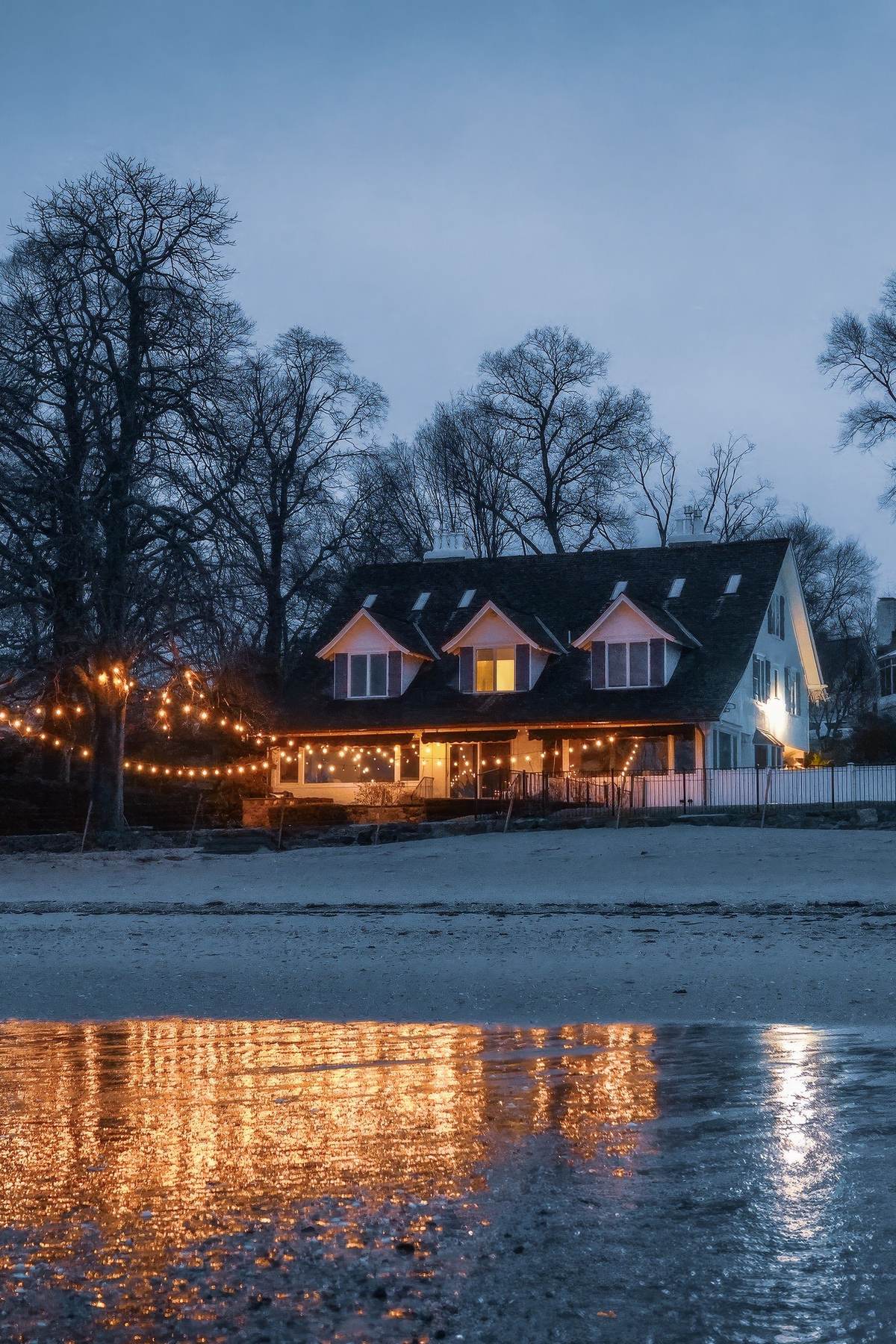 Warm white bulbs running the eave and gable line of a house at dusk, evenly spaced