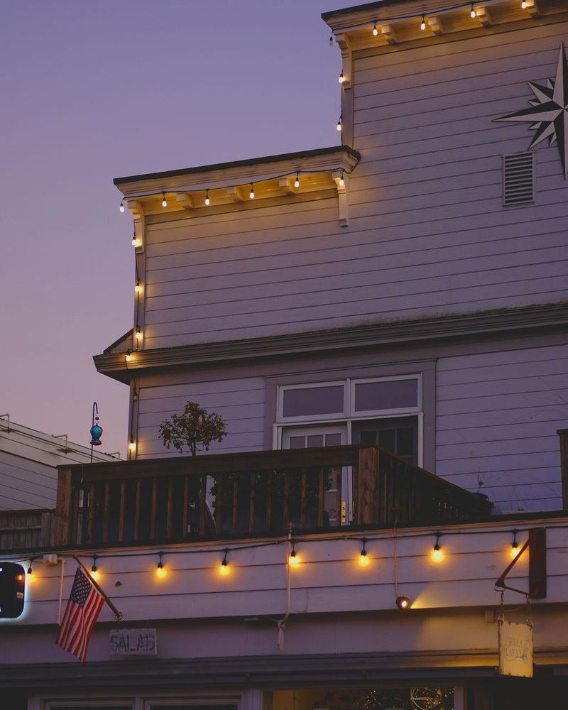 Warm white bulbs running the eave line of a house at dusk