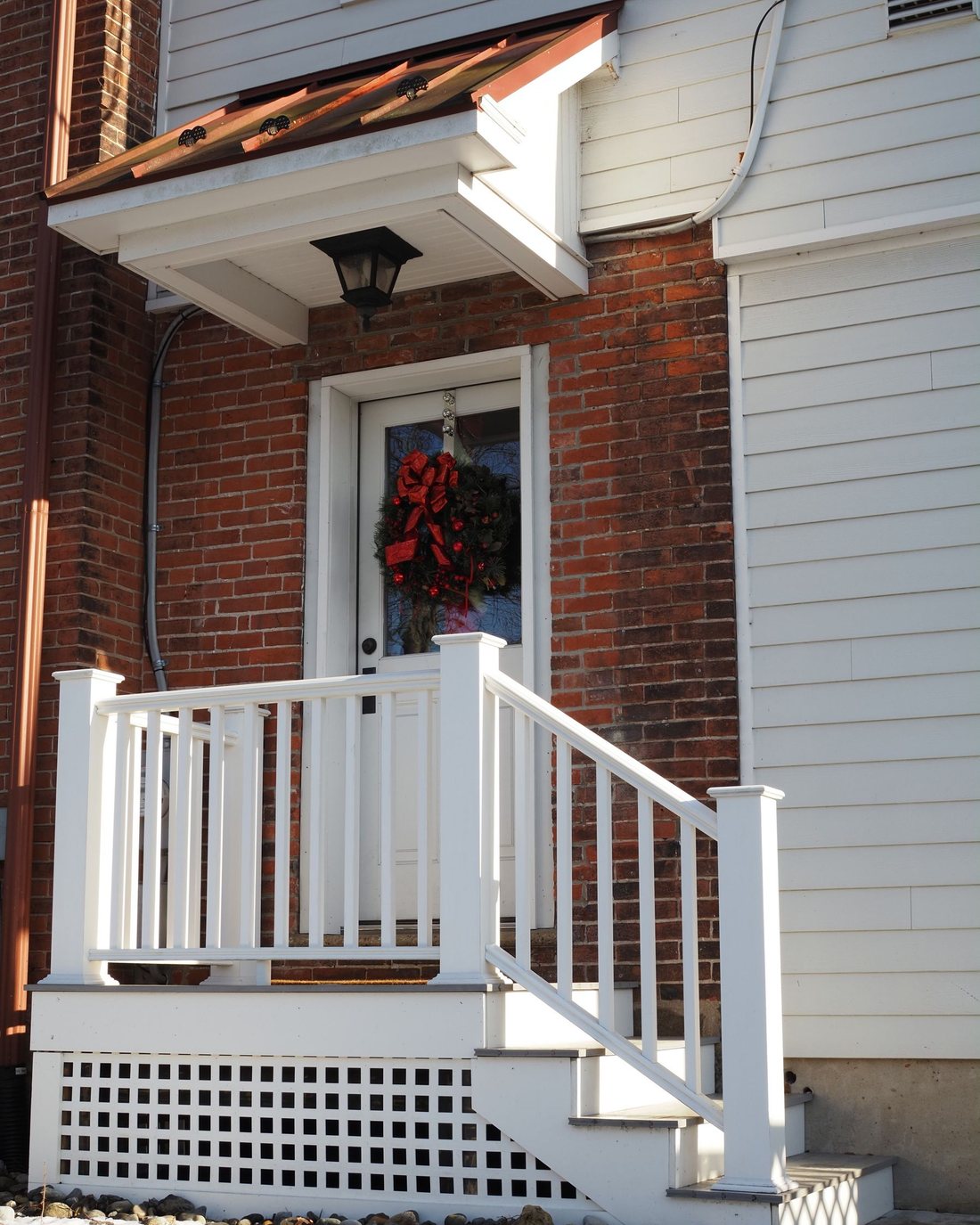 A brick house with a white porch rail and a wreath on the front door