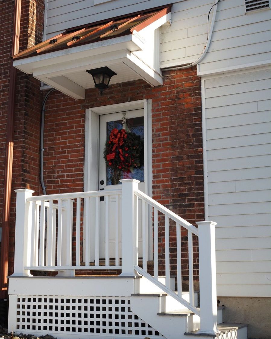 A brick house with a white porch rail and a wreath on the door