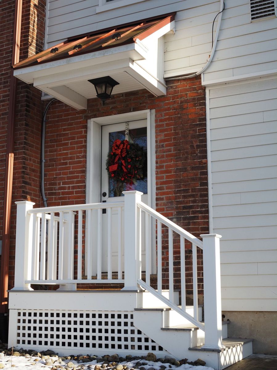 A brick house with a white porch rail and a wreath on the front door