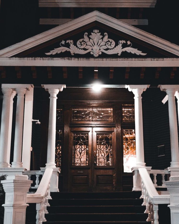 A columned entry lit warm at night with light spilling through the double doors